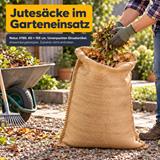 Eine Person mit Handschuhen füllt Laub und Grünschnitt in einen naturfarbenen Jutesack H185, 60 × 105 cm. Daneben stehen Schubkarre und Rechen.